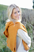 Young blond woman in white turtleneck sweater, with yellow knitted sweater slung over shoulders in nature