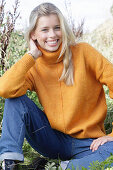 Junge blonde Frau in gelbem Rollkragenpullover und Jeans in der Natur