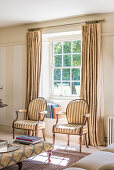 Stühle im antiken Stil vor Fenster mit bodenlangen Leinenvorhängen in hellem Wohnzimmer