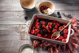 Autumnal spiced and roasted plums and blackberries in a roasting dish, served wih yoghurt
