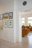 View from hallway with picture collection into living room on a rust colored plush sofa