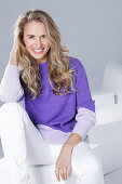 Blonde woman wearing a purple sweater and white trousers