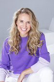 Blond woman wearing a purple sweater and white trousers