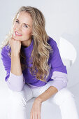Blond woman wearing a purple sweater and white trousers