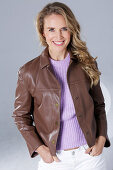 Blonde woman wearing a purple sweater, brown leather jacket and white trousers