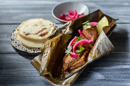 Mexican cochinita pibil dish made of pork wrapped in banana leaf garnished with pickled onion and cilantro