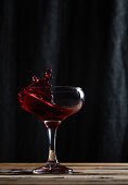 Splashing tasty alcoholic red wine with small drops in transparent wineglass placed on table against black background in modern studio