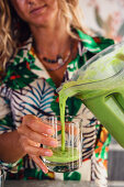 Frau gießt gesunden grünen Smoothie aus Mixer in Glas