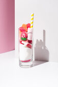 Glass with bunch of sweet gummy candies and white sugar placed near striped straw on pink and white background
