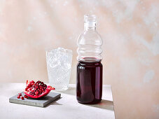 Grenadine in bottle next to a piece of pomegranate
