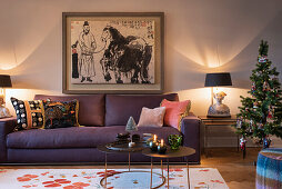 Purple upholstered sofa, artwork above, side tables and small Christmas tree in illuminated living room