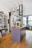 Cooking island with purple fronts, above extractor hood and pendant lights, glass cabinet with glasses