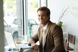 A young businessman sitting in an office wearing a brown blazer
