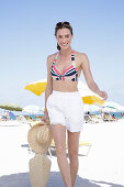 Young brunette woman in a striped bikini top and white shorts on the beach