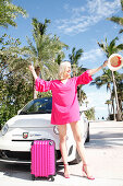 Young blonde woman in a pink summer dress with a matching trolley at the trolley