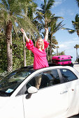 Young blond woman in a pink sundress stands in the skylight opening of a car