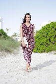 Brunette woman in printed sundress barefoot in the sand