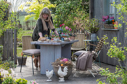 Frau dekoriert Gartentisch mit Osterdekoration, Osternest mit Eiern und Blumentöpfen