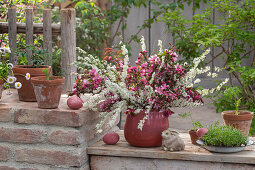 Bouquet of bridal spirea (Spiraea x arguta), tulips (Tulipa) and ornamental apple in clay pot and Easter decoration on terrace