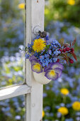 Kleiner Strauß in Eierschale mit Löwenzahn, Zierapfel, Vergissmeinnicht und Hornveilchen (Viola Cornuta) an altem Fenster aufgehängt