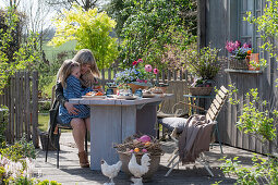 Mutter und Kind beim Osterfrühstück am gedeckten Tisch auf der Terrasse