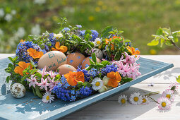 Blumenkranz mit Gänseblümchen, Hyazinthe, Löwenzahn, Traubenhyazinthe, Oregano, Vergissmeinnicht, Veilchen und Garten-Stiefmütterchen (Viola wittrockiana), Ostereier und Schrift