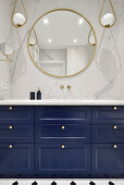 Blue vanity unit, marble tiles above, round mirror and pendant lights in the bathroom