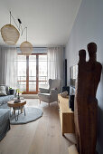 Bright living room with wing chair and balcony, wooden sculpture in the foreground