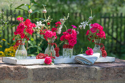 Sträußchen aus Rosen, Prachtkerzen und Etagenzwiebeln in Glasvasen auf Holztablett