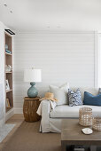 Light-colored sofa with throw pillows and side table with lamp in front of white-painted wooden wall