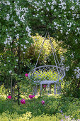 Hängestuhl aus Makramee unter blühender Kletterrose im sommerlichen Garten