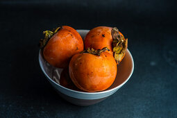 Ripe persimmon fruits in the bowl on stone background