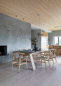 Long dining table with classic chairs in front of concrete wall and fireplace