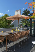 Langer Holztisch mit Obst und Erfrischugnsgetränk, Rattanstühle und Sonnenschirm auf der Dachterrasse