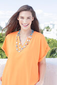 A cheerful young woman wearing an orange summer blouse with a necklace