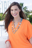 A cheerful young woman wearing an orange summer blouse with a necklace