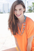 A cheerful young woman wearing an orange summer blouse with a necklace