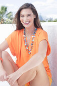 A cheerful young woman wearing an orange summer blouse with a necklace