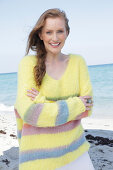 Young, blond woman in yellow jumper with coloured stripes by the sea