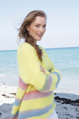 Young, blond woman in yellow jumper with coloured stripes by the sea