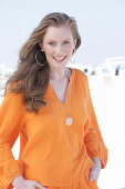 Junge, blonde Frau in orangefarbener Bluse am Strand