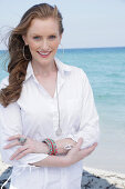 Young, blond woman in white blouse dress by the sea