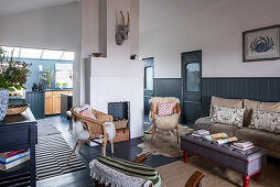 Wicker armchair with sheepskin, sofa, and upholstered coffee table in an open-plan living room with chair rail and wooden paneled wall