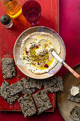 Hummus mit Schwarzkümmel, Pinienkernen, Essblüten und Saaten-Cracker