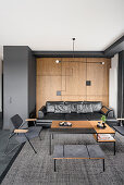 Living room in black and dark brown, wall above leather couch covered with oak veneer