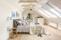 Weißes Schlafzimmer im Dachgeschoss mit Doppelbett und Hängematte rustikaler Boho-Stil, Doppelbett mit mehreren Tagesdecken und Kissen aus Naturstoffen, Hängematte