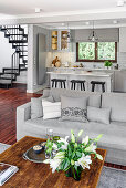 Open living room with light grey upholstered sofa, white grey kitchen and stairs