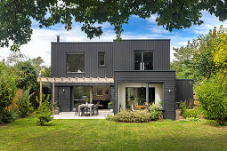 View of 70s house with black façade and terrace from the garden