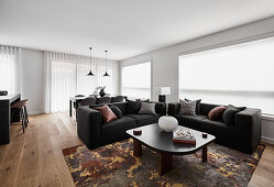 Open plan living room with black sofas, dining area with black wooden table and grey upholstered chairs