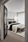 Opulent bedroom in neutral tones with paneled walls, hanging chandeliers, and French doors